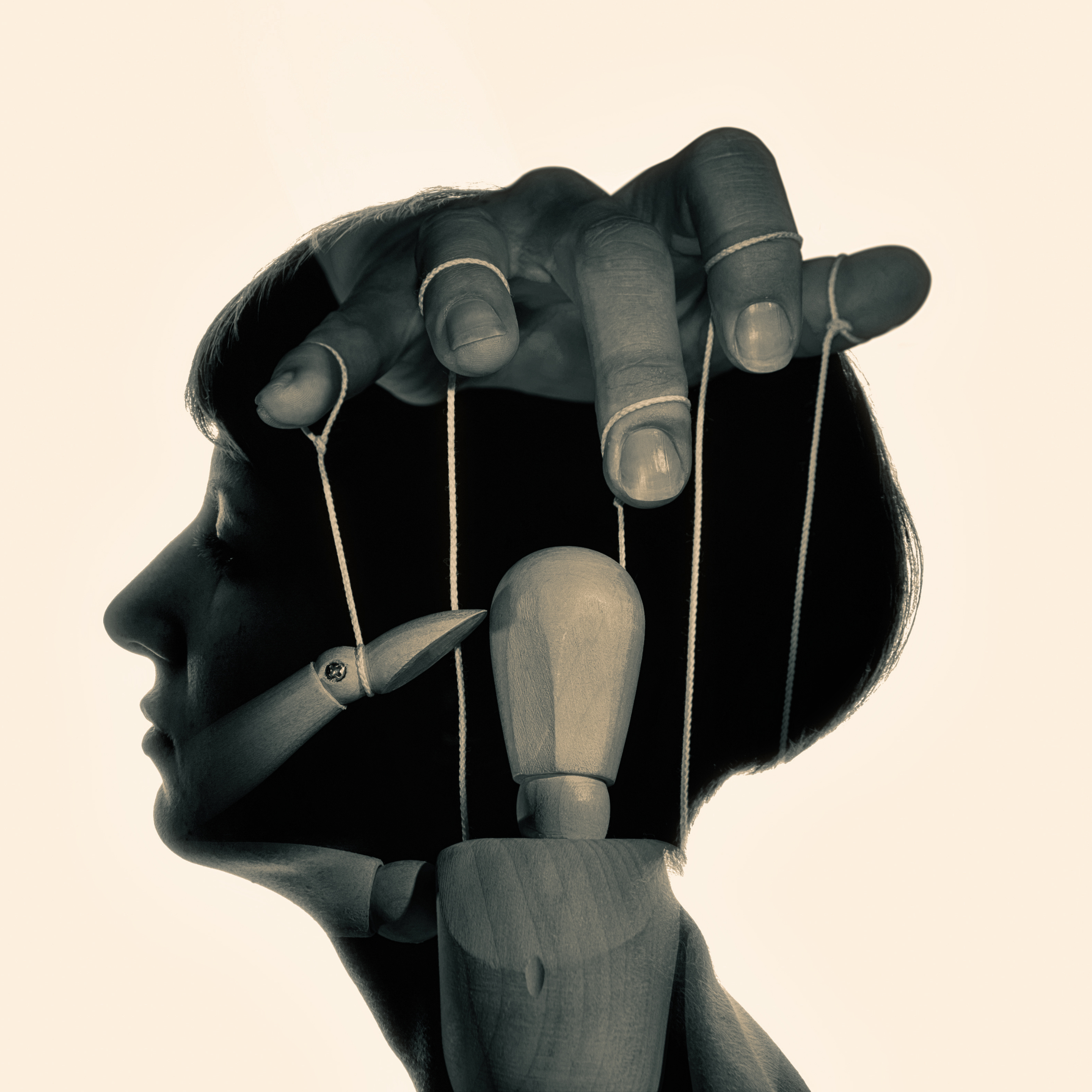 A hand controlling a puppet with strings inside a female head.